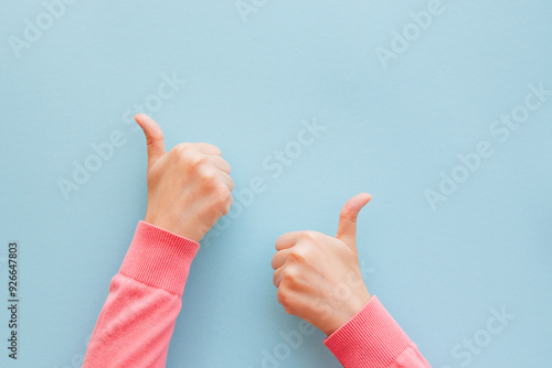 Two woman's hand in pink clothes is showing thumb up on blue background, motivation and success concept