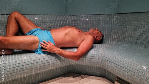 Bild auf Leinwand Man relaxing in a sauna with blue swim trunks in a tiled steam room