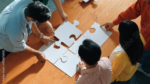 Top view of skilled business people gathering jigsaw piece together.Startup team with casual cloth standing at table while put jigsaw on table. Show unity, cooperation and team working. Convocation. photo