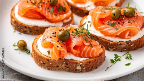 A piece of bread with salmon and capers, placed on a white plate with olives and capers.