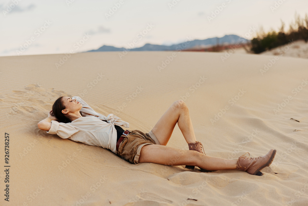 A woman resting in the desert, stretching her legs up in the air on the sandy ground