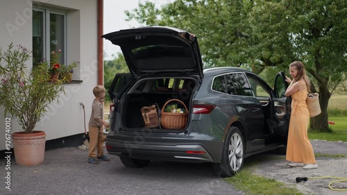 Father charging electric car after grocery shopping in supermarket. Plugging charger into electric vehicle in front of house.