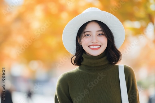 Smiling woman in green sweater and white hat among autumn leaves in a sunny park