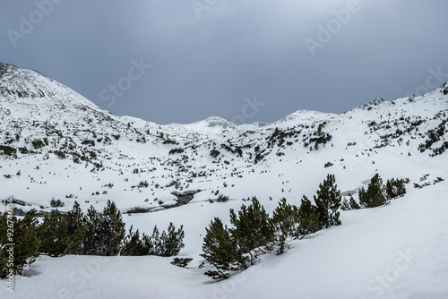 Pirin mountains in early spring. Bunderishka river against Bunderishki chukar peak under stormy sky. Valley under the snow. photo