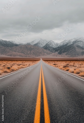Wide open road stretches towards snow-capped mountains under a cloudy sky