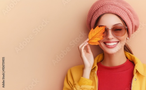 Smiling woman wearing sunglasses and a pink hat holds a leaf against a beige ...