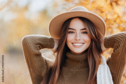 Young woman in a brown sweater and hat poses cheerfully in an autumn park set...