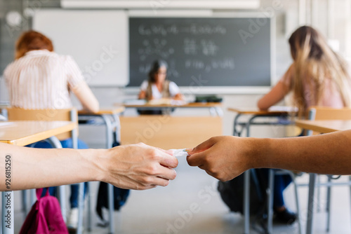 Bilde på lerret Young teenage boy giving cheat sheet to classmate during examination in classroom