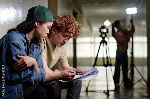 Quadro su tela Two young individuals sitting together and reviewing script in a film production