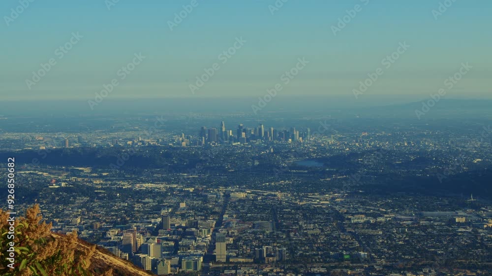 A green mountain in the foreground with the cityscape of Los Angeles in the background. The slight camera movement adds a dynamic feel to the contrast between the natural and urban elements. A green mountain in the foreground with the cityscape of Los Angeles in the background. The slight camera movement adds a dynamic feel to the contrast between the natural and urban elements.