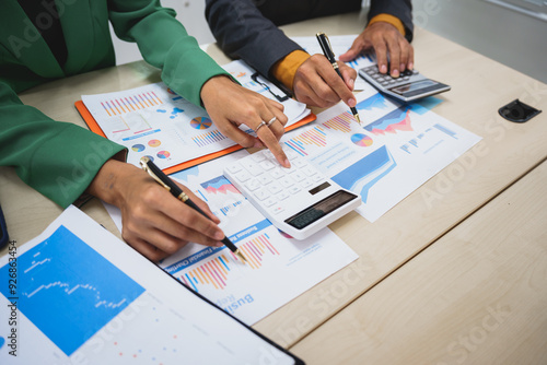 Asian business team engages in a collaborative meeting, financial charts at a desk. Dressed in formal suits, they brainstorm creative ideas to enhance company performance and team cohesion.