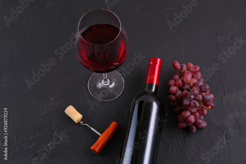 Corkscrew, glass of wine, bottle and grapes on black table, above view photo