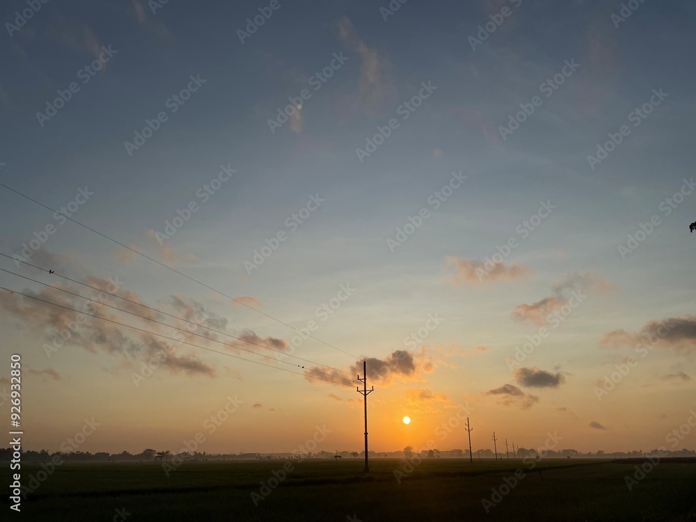Fototapeta premium Silhouette electric pole and high voltage tower.High voltage transmission pole against morning sun in rice fields background.