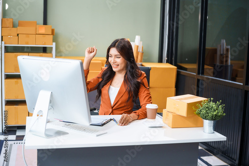 A beautiful businesswoman works at her desk, selling products online. She smiles as she looks at the computer screen, satisfied that her online business has exceeded sales targets.