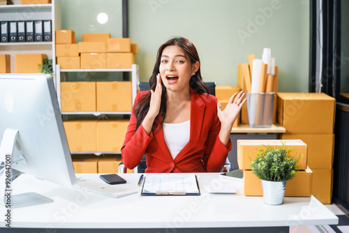 A beautiful businesswoman sits at the table, looking at the computer screen and talking on the phone. She analyzes marketing plans with a smile, feeling happy and successful in her online business.