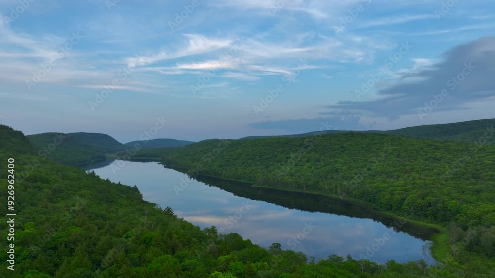 A breathtaking view of Lake of the Clouds at sunset during July, captured by drone footage in the Porcupine Mountains, Upper Peninsula, Michigan. The tranquil lake reflects the serene sky. A breathtaking view of Lake of the Clouds at sunset during July, captured by drone footage in the Porcupine Mountains, Upper Peninsula, Michigan. The tranquil lake reflects the serene sky.