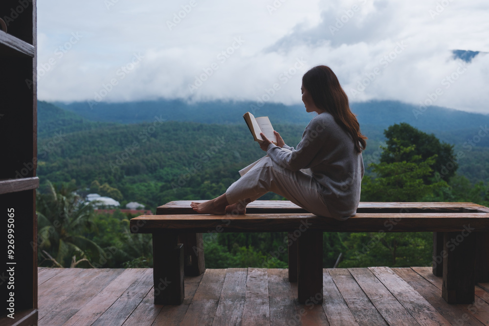 Fototapeta premium A woman reading a book while sitting on wooden balcony with a beautiful mountain views