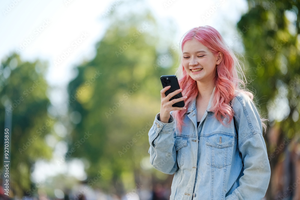 A girl with pink hair is smiling and looking at her cell phone