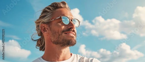  A man with long hair and glasses gazes at the blue sky, surrounded by white, fluffy clouds in the background