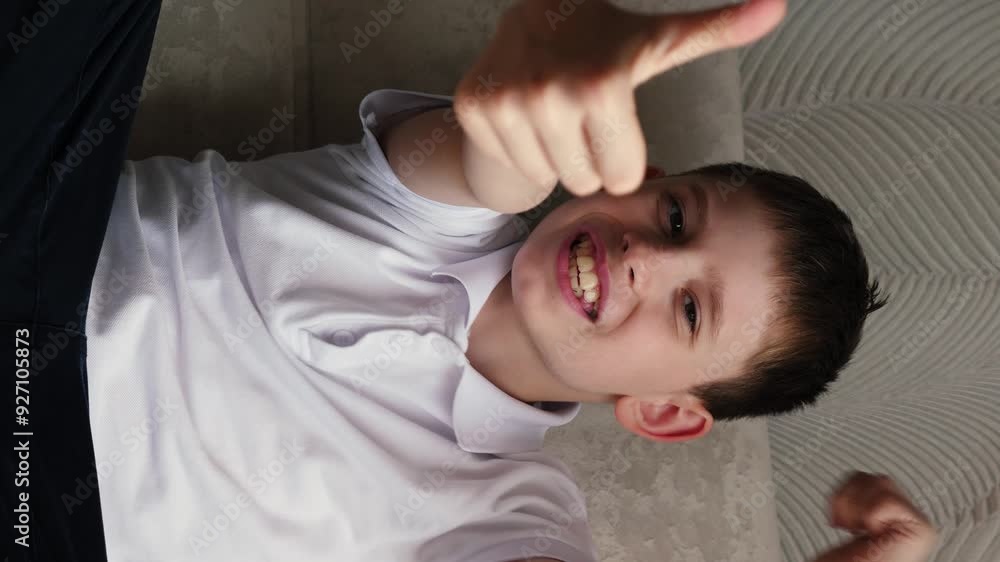portrait of caucasian cheerful boy 10-12 years old showing with hands gesture like or cool sitting on sofa and looking at camera, vertical video portrait of caucasian cheerful boy 10-12 years old showing with hands gesture like or cool sitting on sofa and looking at camera, vertical video
