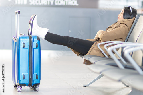 A young woman in a winter coat sits with a suitcase at the airport