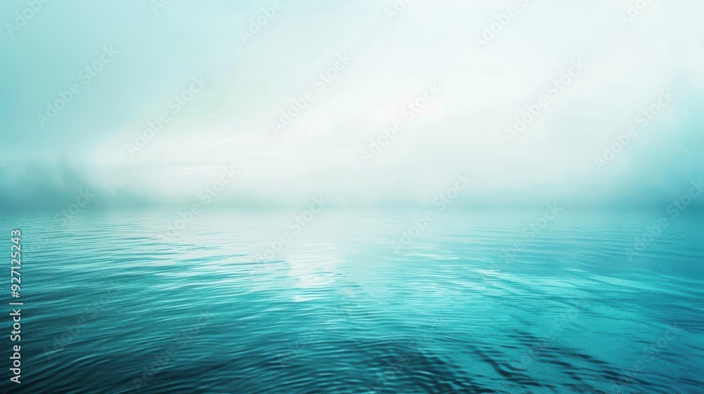 Obraz premium The image shows a tranquil lake scene with fog rolling in over the water. The sky is a soft blue, with wispy clouds and a hint of sunshine breaking through. The water is calm, with gentle ripples caus