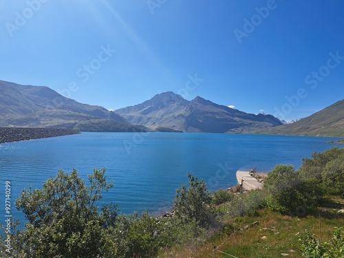 Cette image panoramique met en valeur le barrage du Mont-Cenis, un ouvrage d'art impressionnant qui retient les eaux d'un lac artificiel. Le bleu intense de l'eau contraste avec le vert luxuriant de l