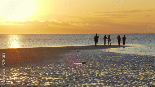Die Sonne senkt sich malerisch am Walakiri Strand auf der Sumba Insel hinter 5 Personen als Silhouetten und zeichnet Strukturen im feuchte Sand