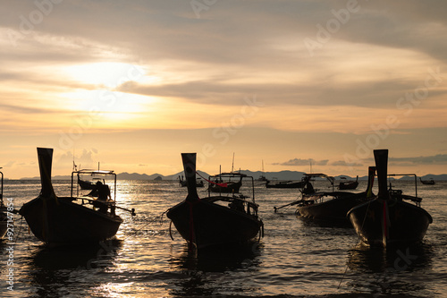 Yellow backlit image of a tourist boat moored on the beach. mountains and fjords Sea waves at the beach under a cloudy sky. Asia. Krabi. Thailand. Evening sunset light.