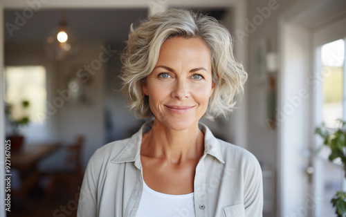 A woman with a short gray hair is smiling and looking at the camera. She is wearing a white shirt and a gray jacket