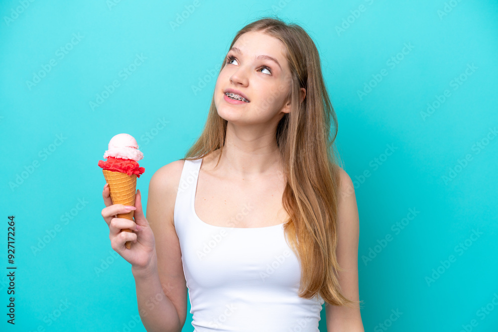 Teenager Russian girl with a cornet ice cream isolated on blue background looking up while smiling Teenager Russian girl with a cornet ice cream isolated on blue background looking up while smiling