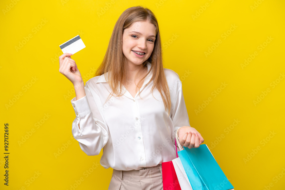 Teenager Russian girl isolated on yellow background holding shopping bags and a credit card Teenager Russian girl isolated on yellow background holding shopping bags and a credit card