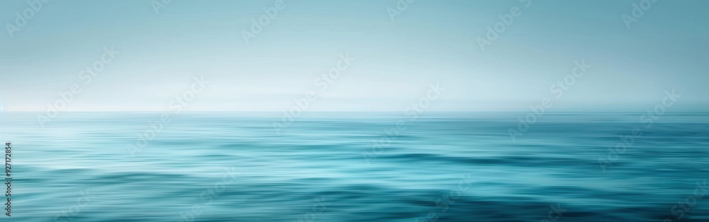 Obraz premium A wide shot of the ocean on a foggy day. The water is a deep blue, with gentle waves rolling across the surface. The sky is a pale blue, blending seamlessly with the sea.
