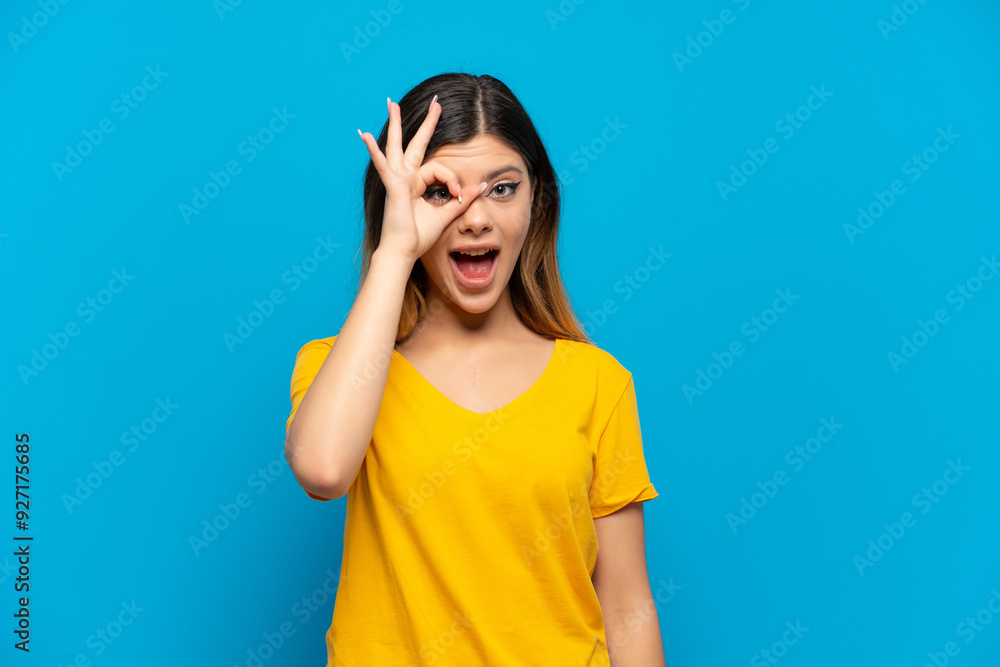 Young Russian girl isolated on blue background showing ok sign with fingers Young Russian girl isolated on blue background showing ok sign with fingers