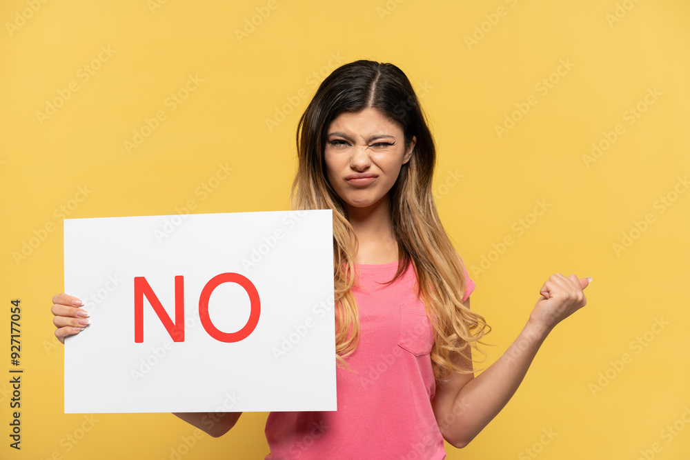 Young Russian girl isolated on yellow background holding a placard with text NO and angry Young Russian girl isolated on yellow background holding a placard with text NO and angry