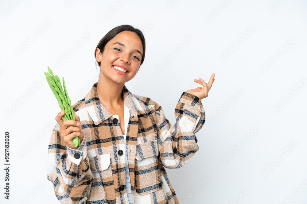 Young hispanic woman holding a green beans isolated on white background extending hands to the side for inviting to come Young hispanic woman holding a green beans isolated on white background extending hands to the side for inviting to come
