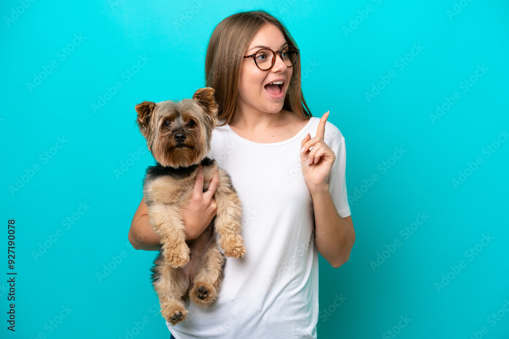 Young Lithuanian woman holding a dog isolated on blue background intending to realizes the solution while lifting a finger up Young Lithuanian woman holding a dog isolated on blue background intending to realizes the solution while lifting a finger up