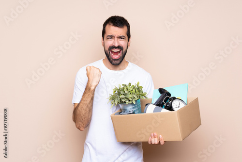 Obraz na plátně Man holding a box and moving in new home over isolated background frustrated by