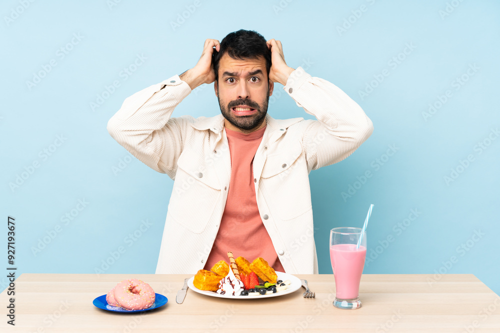Man at a table having breakfast waffles and a milkshake frustrated and takes hands on head Man at a table having breakfast waffles and a milkshake frustrated and takes hands on head