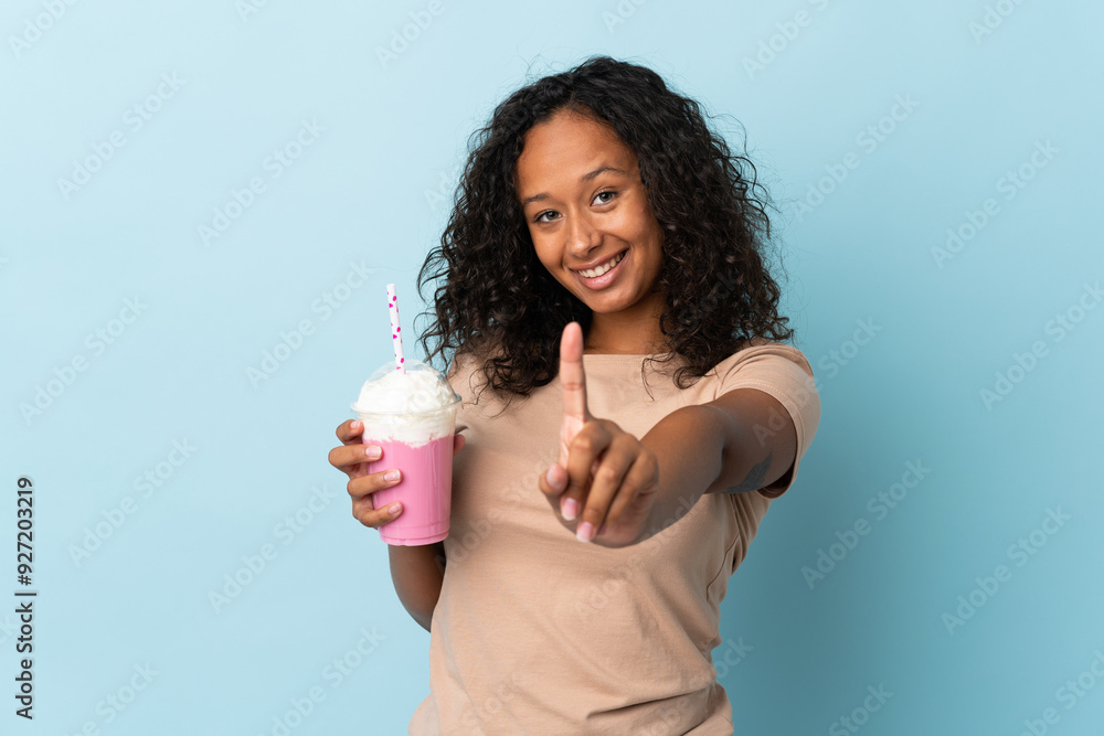 Teenager girl with strawberry milkshake isolated on blue background showing and lifting a finger Teenager girl with strawberry milkshake isolated on blue background showing and lifting a finger
