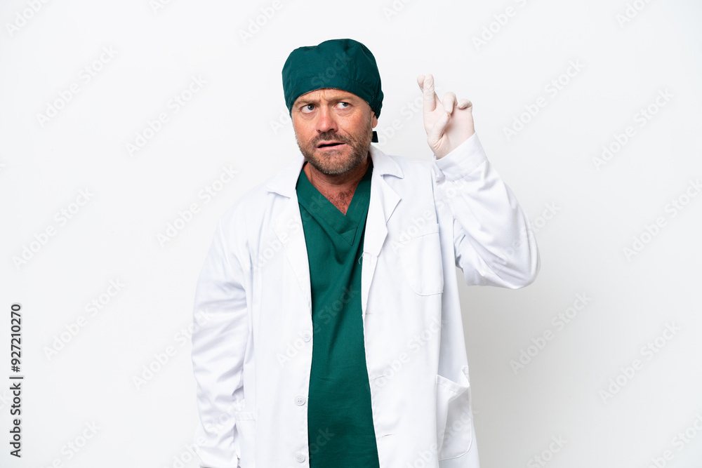 Middle age surgeon in green uniform isolated on white background with fingers crossing and wishing the best Middle age surgeon in green uniform isolated on white background with fingers crossing and wishing the best