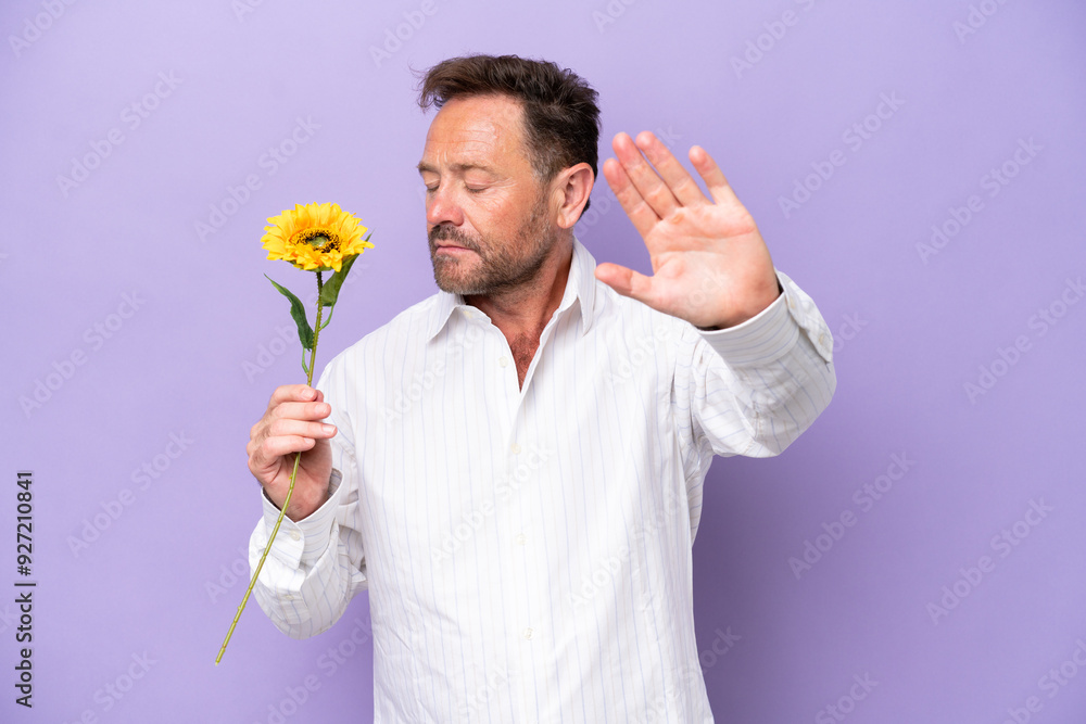 Middle age caucasian man holding sun flower isolated on purple background making stop gesture and disappointed Middle age caucasian man holding sun flower isolated on purple background making stop gesture and disappointed