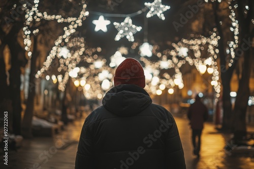 person walks along the street at night, illuminated by Christmas lights