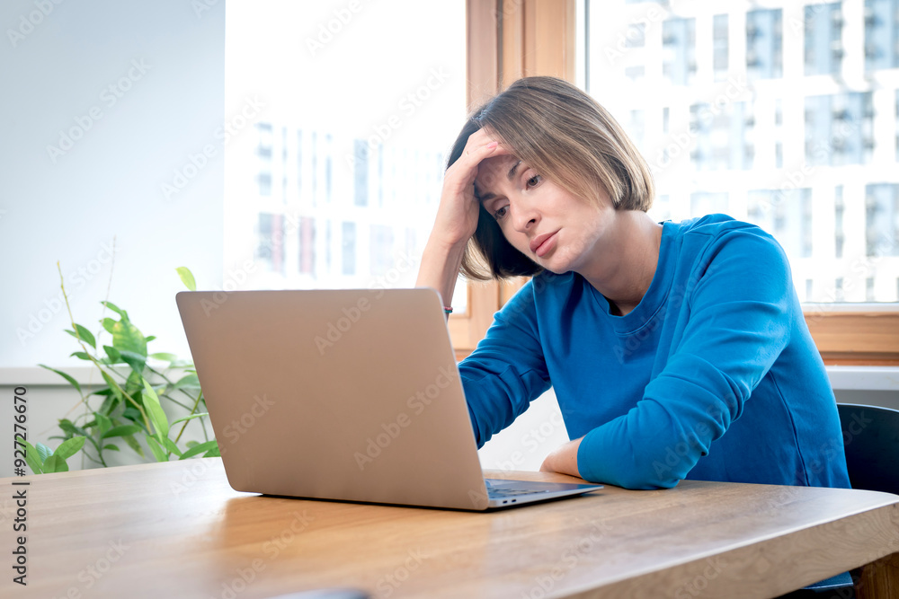 Young attractive woman sitting at the table and working on laptop in the kitchen at home	