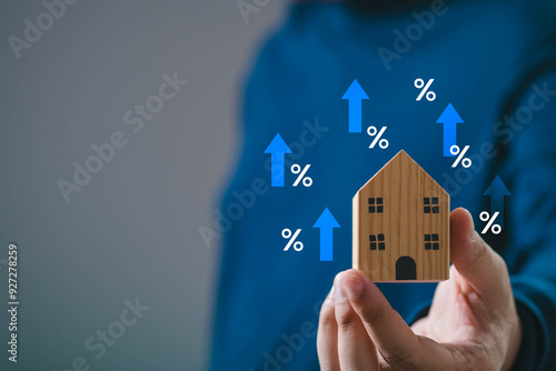 Hand holding wooden house model with upward blue arrows and percentage signs, symbolizing real estate market and mortgage rate increase. photo