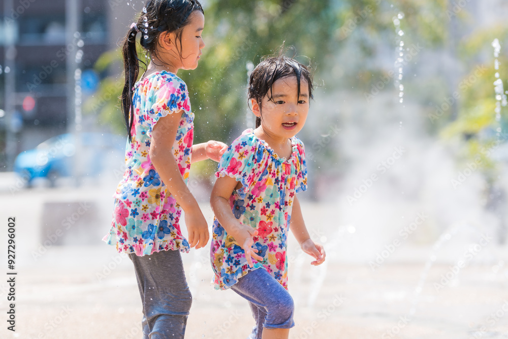Naklejka premium 夏の広場の噴水で水遊びをする女の子