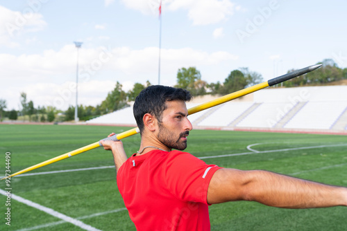 An athletic man throws the javelin in the stadium.