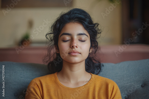 Serene Indian Girl Meditating on a Couch at Home: Close-Up of Deep Breathing Yoga Exercise for Relaxation and Mental Health