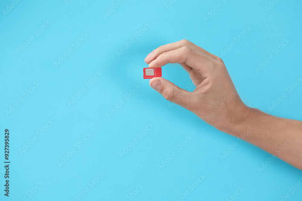 Fototapeta premium Man with SIM card on light blue background, closeup. Space for text