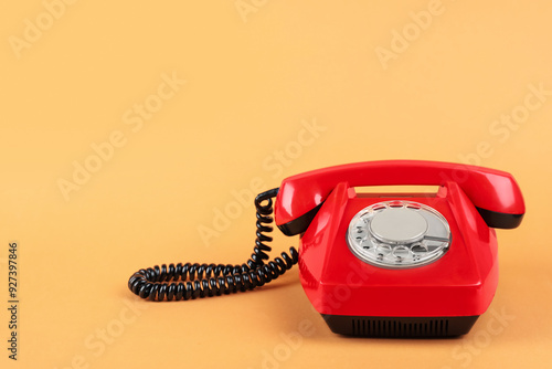 One red telephone with handset on pale orange background, space for text